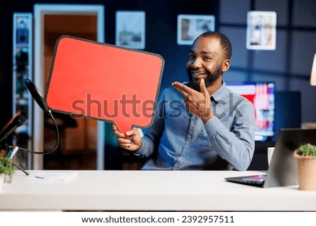 Happy man comissioned by brand to film sponsored content, holding empty copy space sign in hand, talking to audience. Trending media star using cardboard bubble speech cutout to do promotion to fans Royalty-Free Stock Photo #2392957511