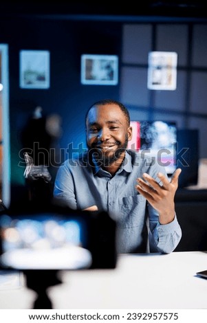 Smiling content creator using professional recording camera and microphone to do livestream and talk with fans. Online streamer using video production gear to do live broadcast for his subscribers Royalty-Free Stock Photo #2392957575