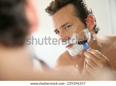Mature handsome man shaving in front of mirror Royalty-Free Stock Photo #239296357