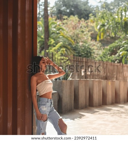 Urban vibes: stylish latino girl in jeans and little top posing against copper wall under sunlight, with big copy space