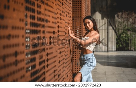 Urban vibes: stylish latino girl in jeans and little top posing against copper wall under sunlight, with big copy space