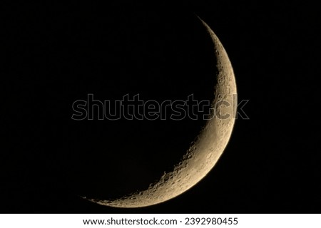 Crescent Moon on dark black sky background, shot from surface of earth with very long telephoto lens. Grey white moon glowing at clear sky.