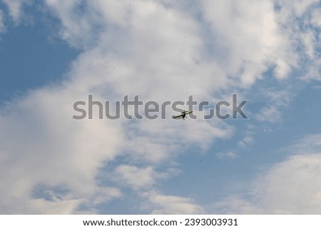 A light aircraft flies below a thin cloud cover in the sky