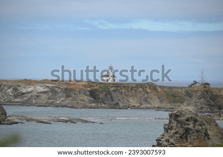 A beautiful scenic view of a lighthouse out on a piece of land surrounded by water.  Picture taken from a distance.