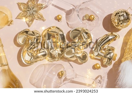 Happy New Year festive background, golden inflatable balls in shape 2024 on pale pink background, sparkling wine champagne bottle, wine glasses with Christmas holiday shiny decor. Star filter effect