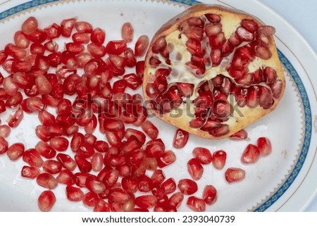 Pomegranate seeds and pome granate cut in half on a plate Royalty-Free Stock Photo #2393040739