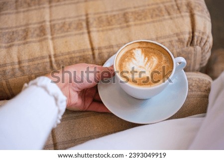 A woman in white clothes holds her delicious coffee in a white cup