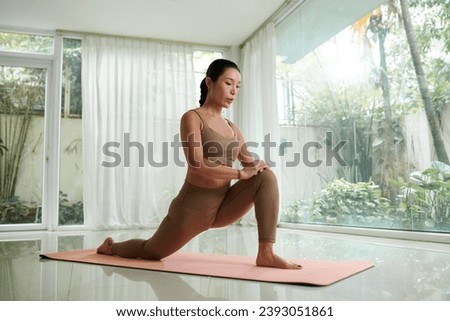 Fit young Vietnamese woman doing hip flexors stretch exercise Royalty-Free Stock Photo #2393051861