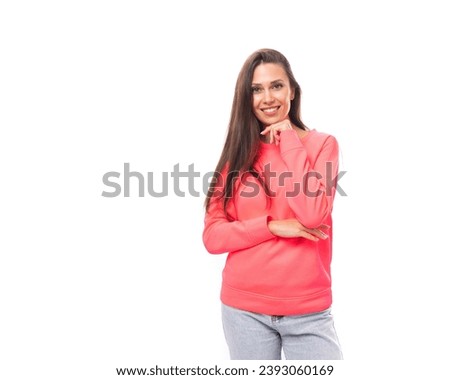 pretty young brunette caucasian woman with straight hair is dressed in a pink sweatshirt and jeans on a white background with copy space