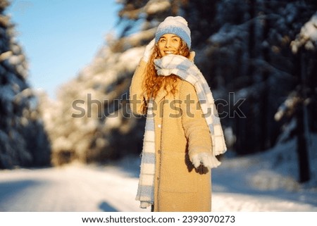 Young woman enjoys a beautiful winter day in the forest. She walks and enjoys the snow. Winter time. Cold weather. Holidays, rest, travel concept.