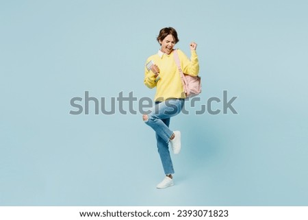 Full body young woman student wear casual clothes sweater backpack bag hold books do winner gesture celebrate clenching fists isolated on plain blue background. High school university college concept Royalty-Free Stock Photo #2393071823
