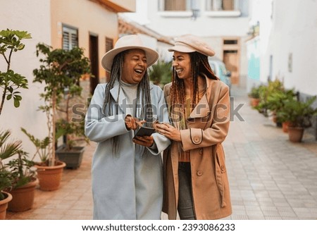 Happy african mother and daughter having fun together using mobile phone in the city during winter time - Travel and vacation concept