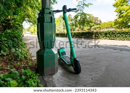 Green colored electric scooter parked against a metal lamppost