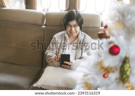 Senior people stay at home alone on Christmas holidays concept. Happy asian elder woman lifestyle with modern technology using mobile phone for online social media.