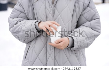 Close-up of a paper white glass of coffee in a woman's hands outdoors in winter      
