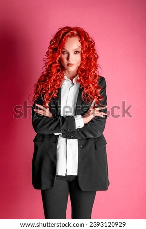 Studio photo of a young business woman in a black suit and white shirt on a pink background. A red haired businesswoman.