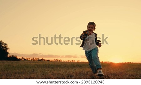 Dream kid Joyful little boy running at sunset. Kid is running across field. Child boy runs through green grass in sun. Childhood dream happiness concept. Happy child playing in nature. Happy family.