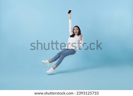 Young asian teenage girl happy hand holding mobile phone floating in mid-air isolated on blue background. Fast internet concept. Royalty-Free Stock Photo #2393125733