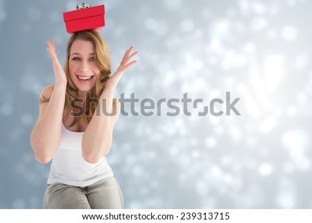 Smiling woman balancing christmas gift on her head against light design shimmering on silver