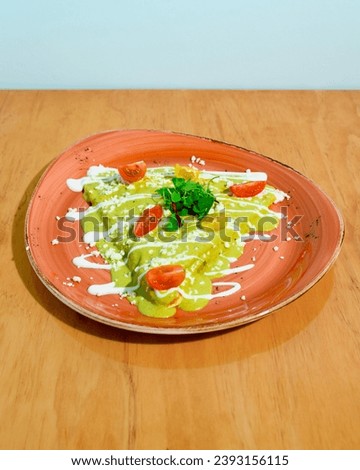 A vibrant plate of green enchiladas garnished with sour cream, cheese, and fresh herbs Royalty-Free Stock Photo #2393156115