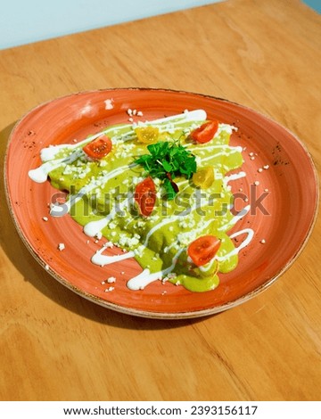 A vibrant plate of green enchiladas garnished with sour cream, cheese, and fresh herbs Royalty-Free Stock Photo #2393156117