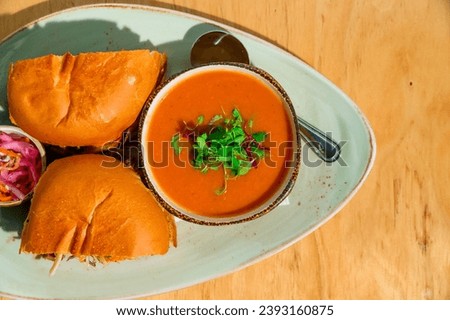 Creamy tomato soup garnished with microgreens, paired with toasted slider buns and pickled onions on an oval plate Royalty-Free Stock Photo #2393160875