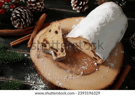 Holiday food Christmas Stollen (Christstollen in Germany) without marzipan over wooden plate with powdered sugar or icing sugar, pinecone, cinnamon, snowflake on black wood plank table background.