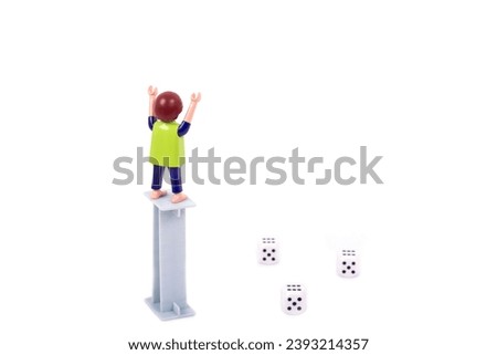 
Gambling concept. A plastic figure stands on a gray pillar with his hands raised high and looks forward to a successful throw of white dice and a win. White background. View from above. 