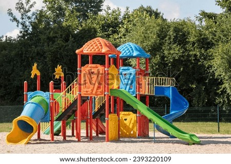 Outdoor playground equipment with slides. Colorful children playground, exercise kid, activities in outdoor public park surrounded by green trees. Royalty-Free Stock Photo #2393220109