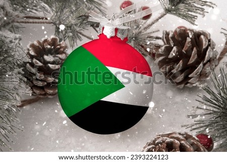 Christmas ball with the flag of Sudan, decorates the snow tree with snowfall. The concept of the Christmas and New Year holiday