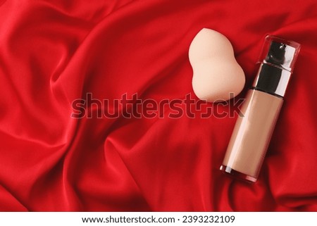 Makeup sponge and skin foundation on red cloth, flat lay. Space for text