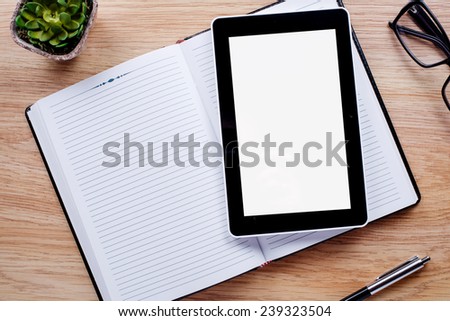 Flower pot, glasses, pen, notebook emphasizing copy space on the tablet screen on light brown desktop