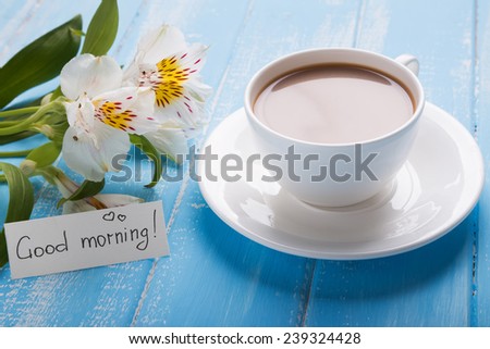 Cup of coffee with milk and alstroemeria flowers on the blue wooden table