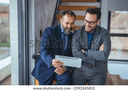 Two happy business colleagues at meeting in modern office interior. Successful mature boss in a conversation with young employee in boardroom. Marketing team of two businessmen discussing 