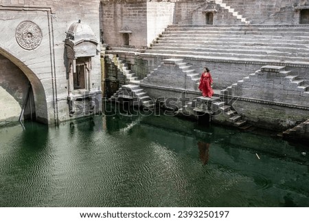 Woman dressed in red on the stairs and water of Toorji Ka Jhalra in Jodhpur in Rajasthan, India. The blue city Royalty-Free Stock Photo #2393250197