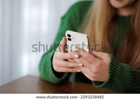 a young girl writes a message on the phone while sitting at the table, working online, chatting