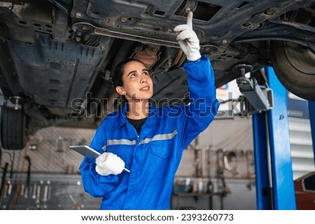 Auto mechanic in blue uniform are repair and maintenance auto engine is problems at car repair shop. Professional Repairman is Wearing Gloves and Using a Ratchet Underneath the Car.