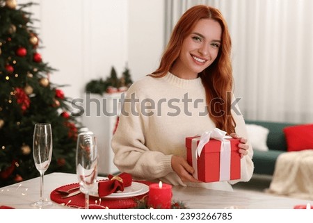 Beautiful young woman with Christmas gift at served table in room