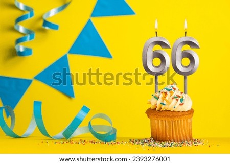Lighted birthday candle number 66 - Yellow background with blue pennants Royalty-Free Stock Photo #2393276001