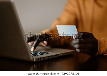 Cropped picture of a multicultural man holding a credit card while typing on a laptop. Hands holding a credit card and typing on a keyboard.