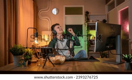Young man teenager play video games on pc computer while streaming to social media or internet online playtrough walktrough video male gamer having fun at home wear headphone happy winning copy space
