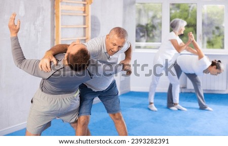 Senior man train in pair with middle-aged coach to strike and reflect blows of enemy. Intense moment as two individuals engage in self-defense training, showcasing skill, reaction, repulse Royalty-Free Stock Photo #2393282391