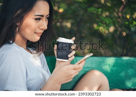Asian Woman use smartphone drinking coffee hand holding hot disposable cup in green park. Banner Happy Relax asian woman smiling face at outdoors garden. Young women enjoy nature with copy space