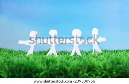 Paper group of people holding hands on green grass on blue background