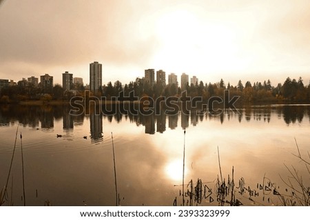 Buildings and sun reflecting onto Lost Lagoon in Stanley Park, Vancouver on a foggy day.
