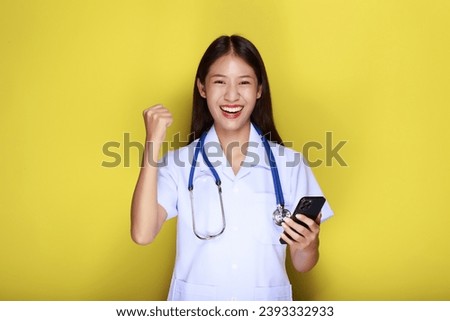 Portrait of a beautiful young woman in a yellow background, Asian woman poses with a cell phone while wearing a doctor's uniform and a stethoscope.