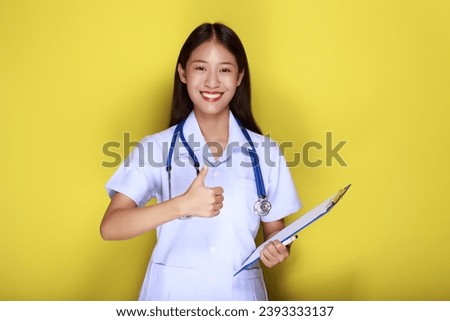 A young woman wearing a doctor's uniform poses with a thumbs up and hangs a medical stethoscope, Portrait of a beautiful young woman in a yellow background, 