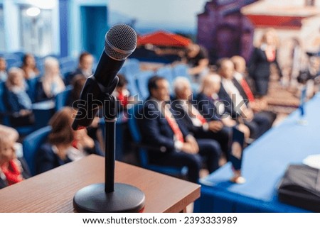 Businesspeople at conference. Blurred photo. Focus on microphone. Royalty-Free Stock Photo #2393333989