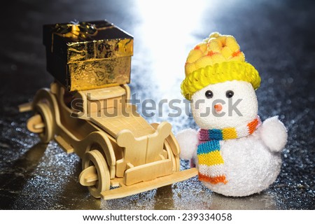 Christmas snowman toy and old vintage wooden automobile with golden or yellow gift box on silver or metal grunge surface with backlight from behind