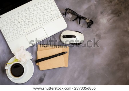 On the office table there is a laptop, a computer mouse, a notepad, a pen, glasses, accessories for working in the office.  Place to copy text, top view.  Cup of coffee, coffee break.